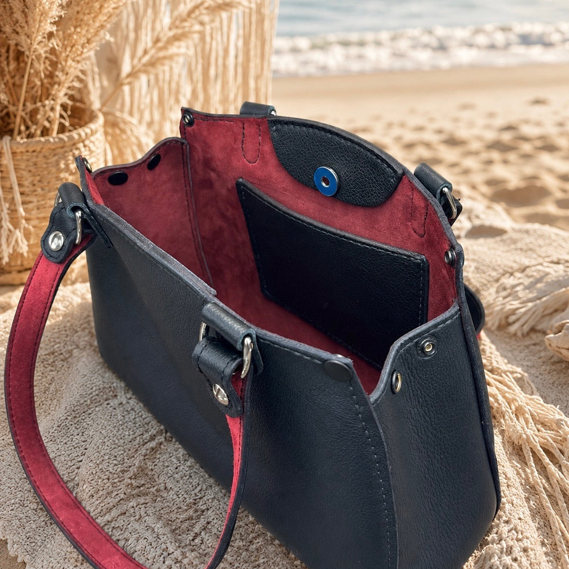 Open black handbag showing red interior, inner pocket, and snap closure