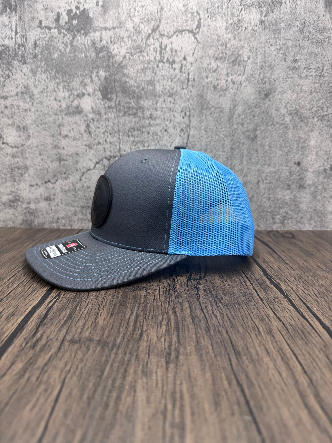 Angled side view of charcoal front and bright blue mesh Hammerhead Shark leather patch hat